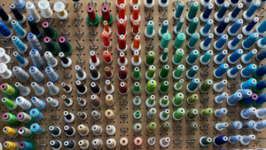 Assortment of colorful spools of thread arranged in rows on a pegboard used for custom embroidery.